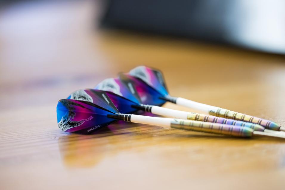 Drei Dartpfeile mit bunten Flights Drei Dartpfeile mit bunten Flights liegen auf einem Holztisch.