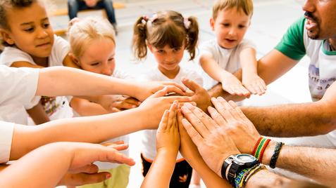 Kinder und Erwachsene legen ihre Hände in einem Kreis zusammen, symbolisieren Zusammenarbeit und Gemeinschaft.